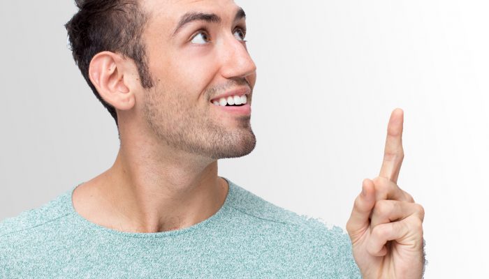 Closeup portrait of smiling young handsome man looking and pointing upwards. Isolated view on grey background.